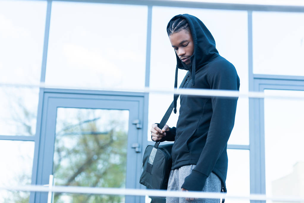 vue latérale du jeune homme afro-américain tenant un sac de sport et regardant vers le bas sur la rue
 - Photo, image