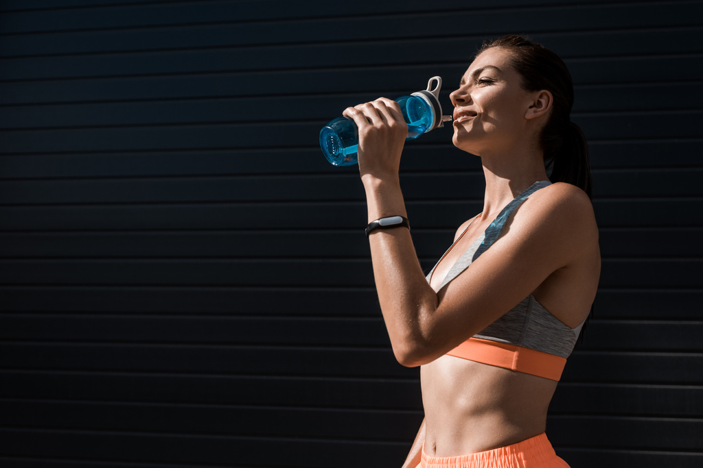 athletic woman with fitness tracker drinking water from sports bottle - Photo, Image