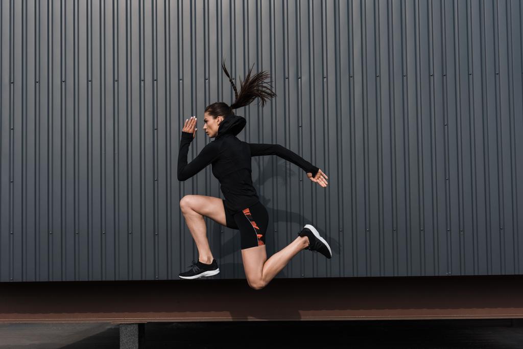 athletic woman in black thermal clothes jumping in city - Photo, Image