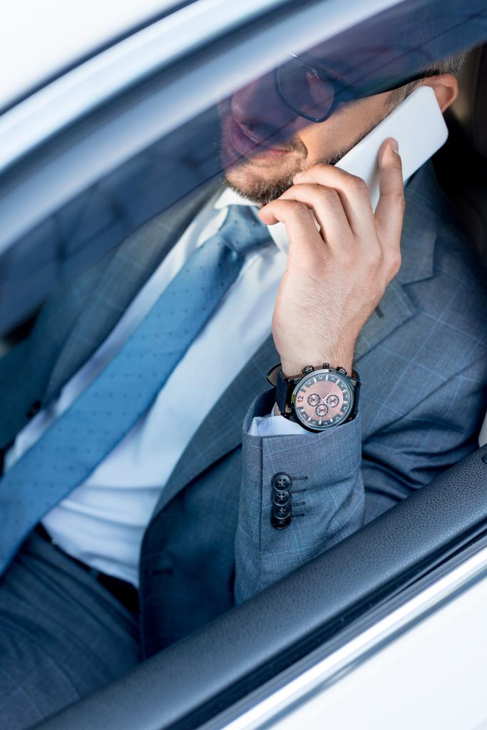 vista parziale di un uomo d'affari sorridente con gli occhiali che parla sullo smartphone mentre guida l'auto
  - Foto, immagini
