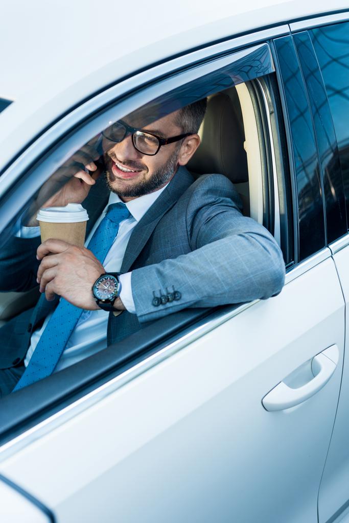 sonriente hombre de negocios con café para ir a hablar en smartphone en coche
  - Foto, imagen