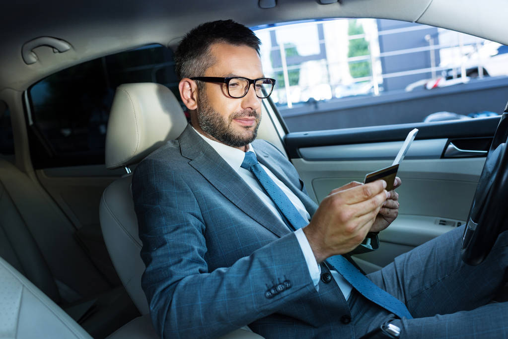 вид сбоку сидящего в машине бизнесмена с планшетом и кредитной картой
 - Фото, изображение