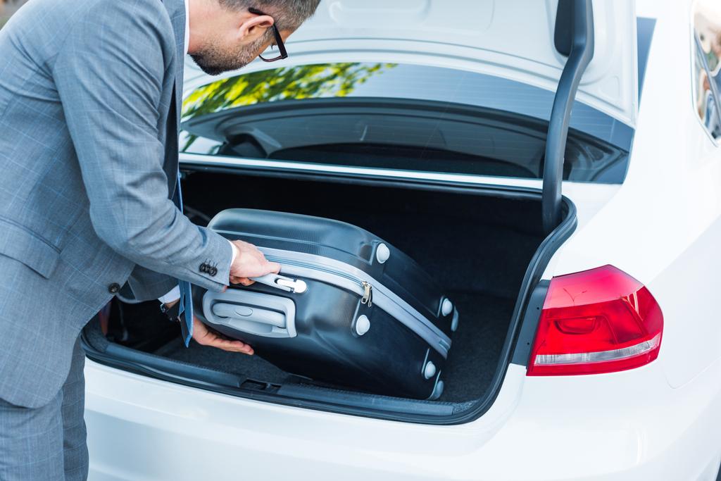 частковий вид на бізнесмена, який поклав багаж у машину на парковці
 - Фото, зображення