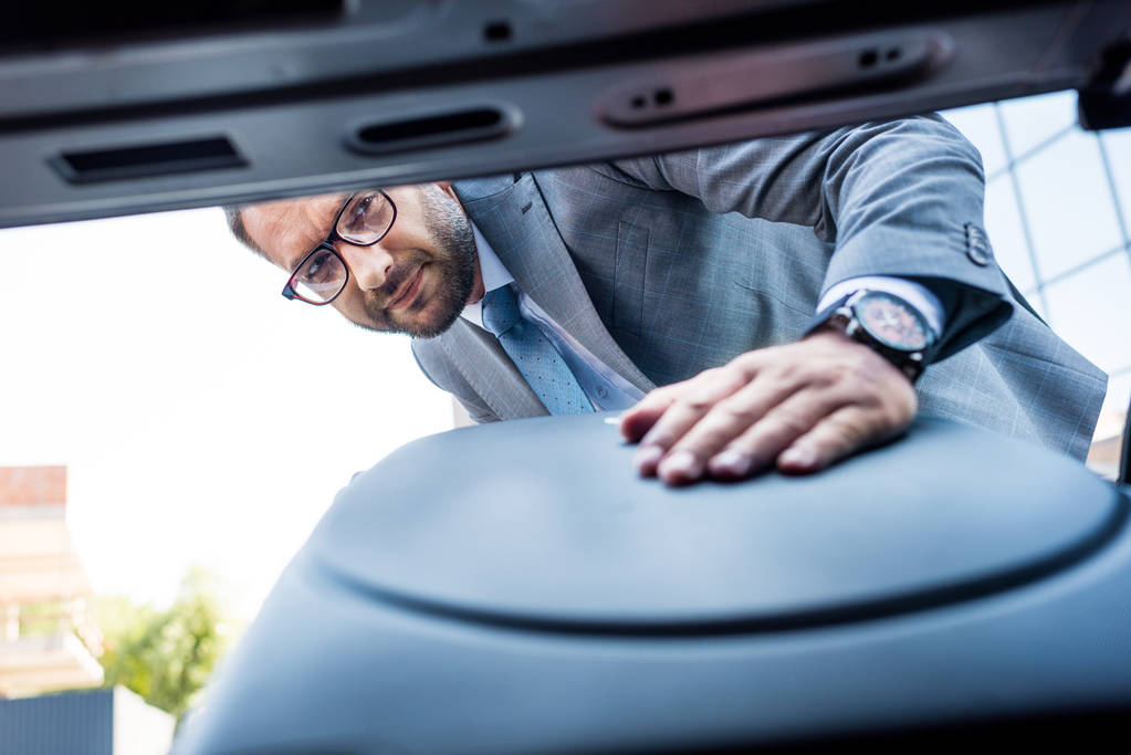 Selektivní fokus podnikatel v brýlích uvedení zavazadla do auta na parkovišti - Fotografie, Obrázek