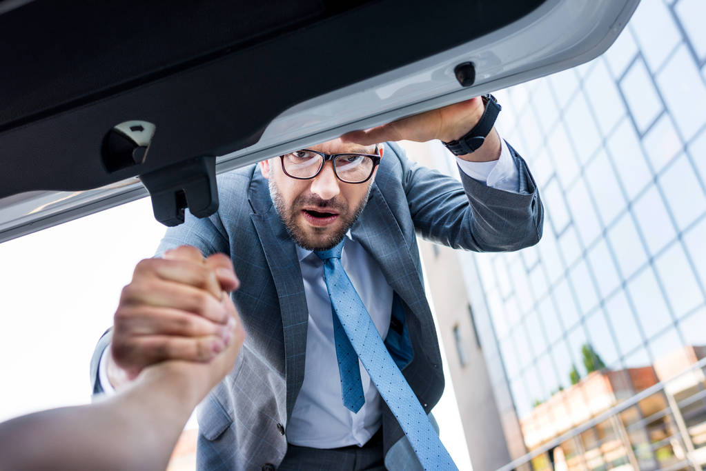 partial view of businessman holding hand of man in luggage boot of car - Photo, Image