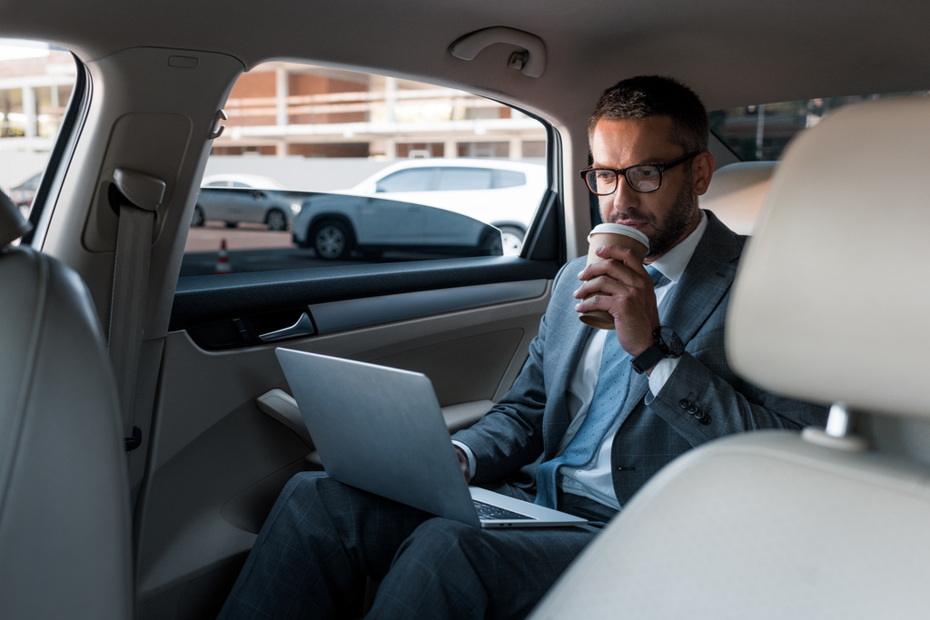 бизнесмен в очках с кофе идти с помощью ноутбука в машине
 - Фото, изображение