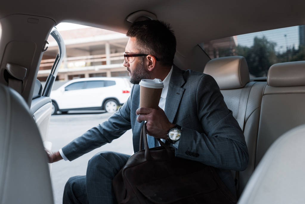 ドアを開けると車の中に座って行くコーヒーを持ったビジネスマン - 写真・画像