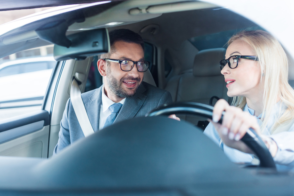 portrait of blonde businesswoman in eyeglasses driving car with colleague near by - Photo, Image
