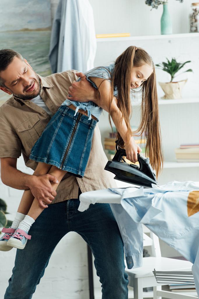Vater trägt ungehorsame Tochter und sie will zu Hause Kleider bügeln - Foto, Bild