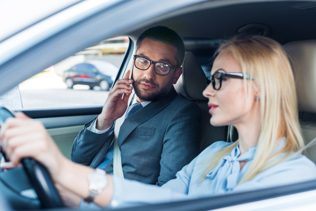 επιλεκτική εστίαση του επιχειρηματίας οδήγηση αυτοκινήτου ενώ συνάδελφος μιλάμε για το smartphone κοντά από στο κάθισμα επιβατών - Φωτογραφία, εικόνα