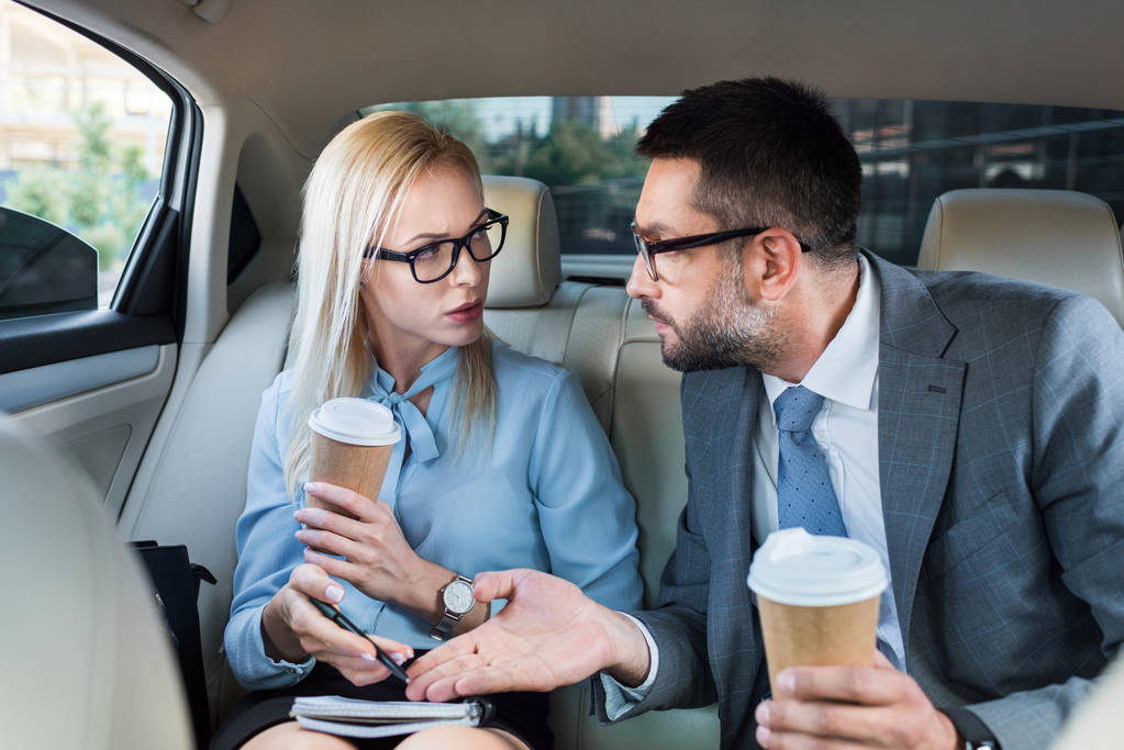 portrait of business people with coffee to go discussing work on back seats in car - Photo, Image