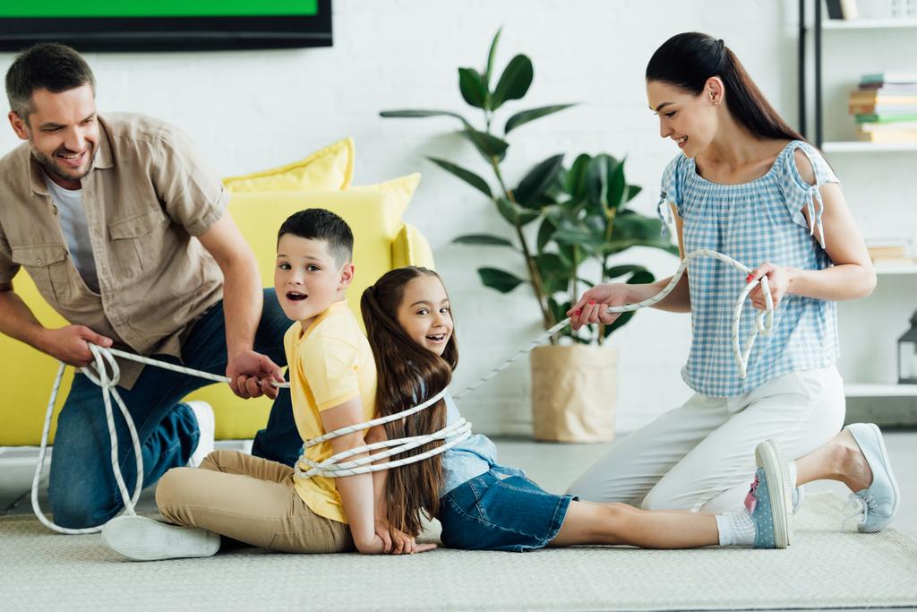 усміхнені батьки зв'язують дітей мотузкою вдома, концепція батьківства
 - Фото, зображення