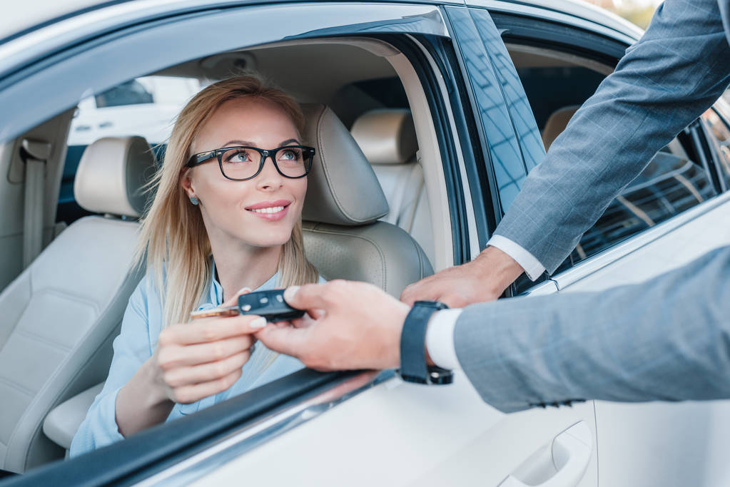 partial view of businessman giving car keys to smiling colleague at driver seat in car - Photo, Image