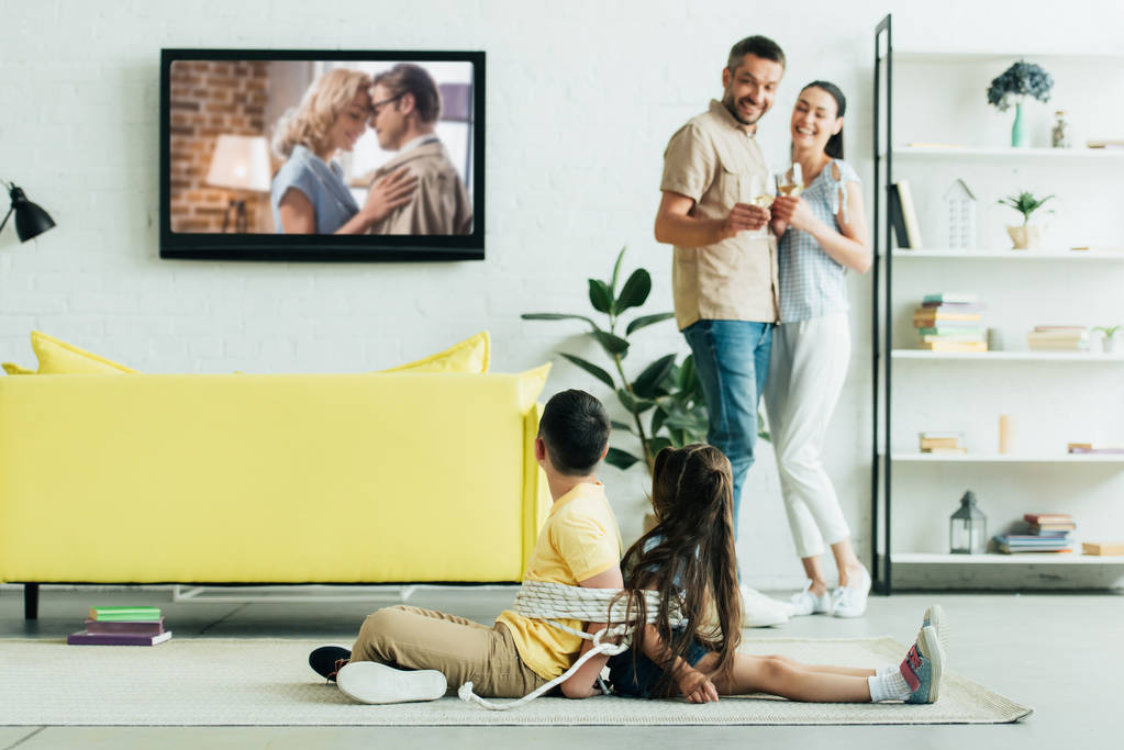 батьки відпочивають з шампанським і неслухняними дітьми, які сидять пов'язані з мотузкою на підлозі вдома
 - Фото, зображення