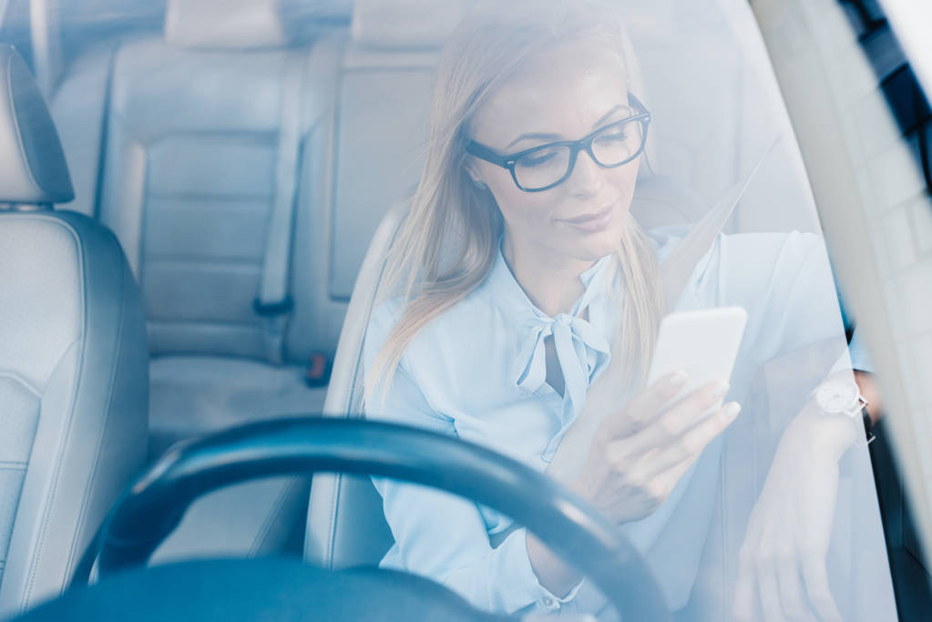 portrait of businesswoman in eyeglasses using smartphone in car - Photo, Image