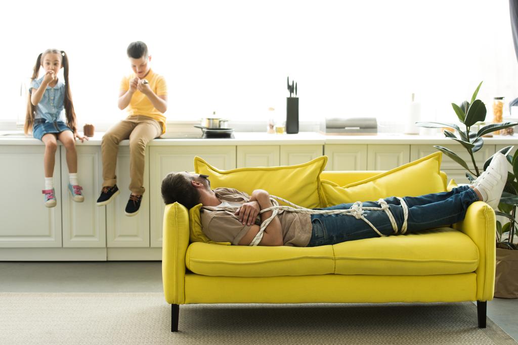 bambini che mangiano dessert e papà sdraiati sul divano a casa, concetto di genitorialità
 - Foto, immagini