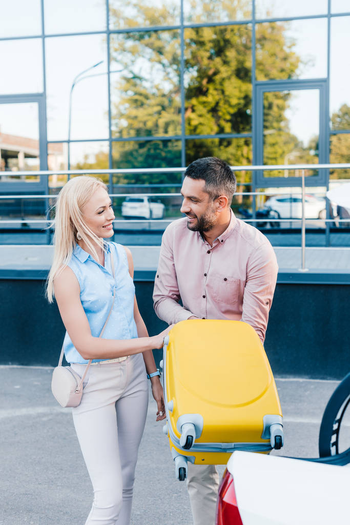 usměvavý manželský pár dát zavazadla do auta na parkovišti - Fotografie, Obrázek