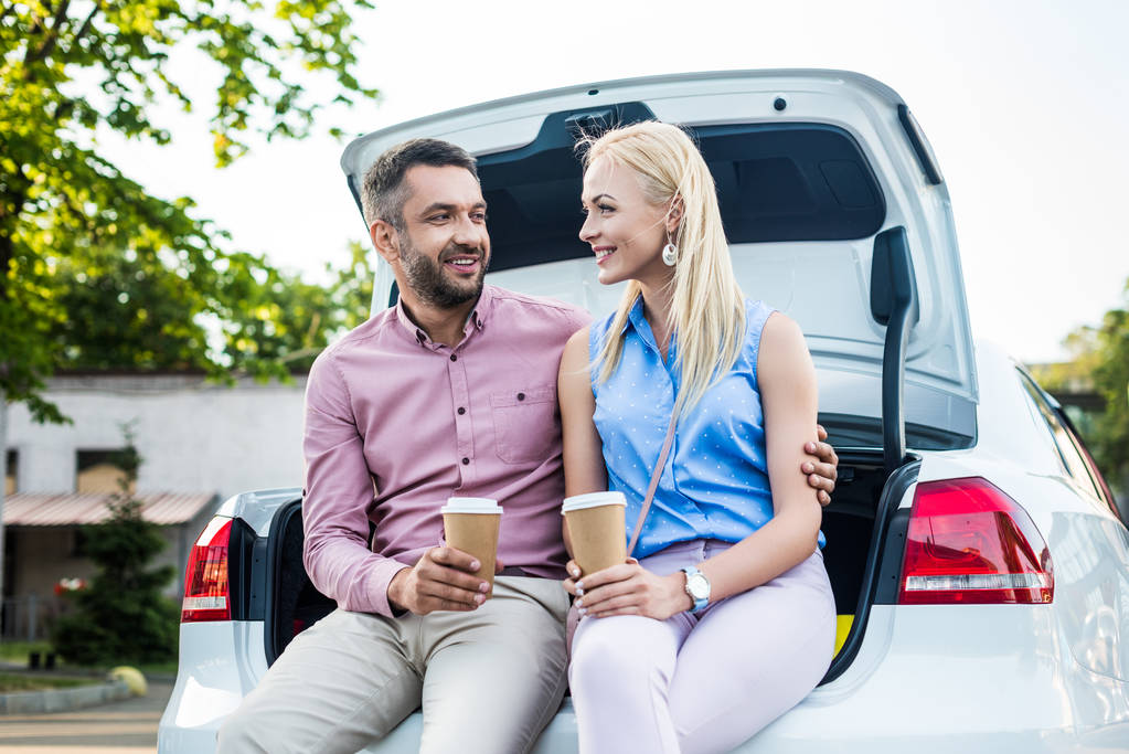 retrato de pareja sonriente con café para ir sentado en el coche y mirarse el uno al otro
 - Foto, Imagen