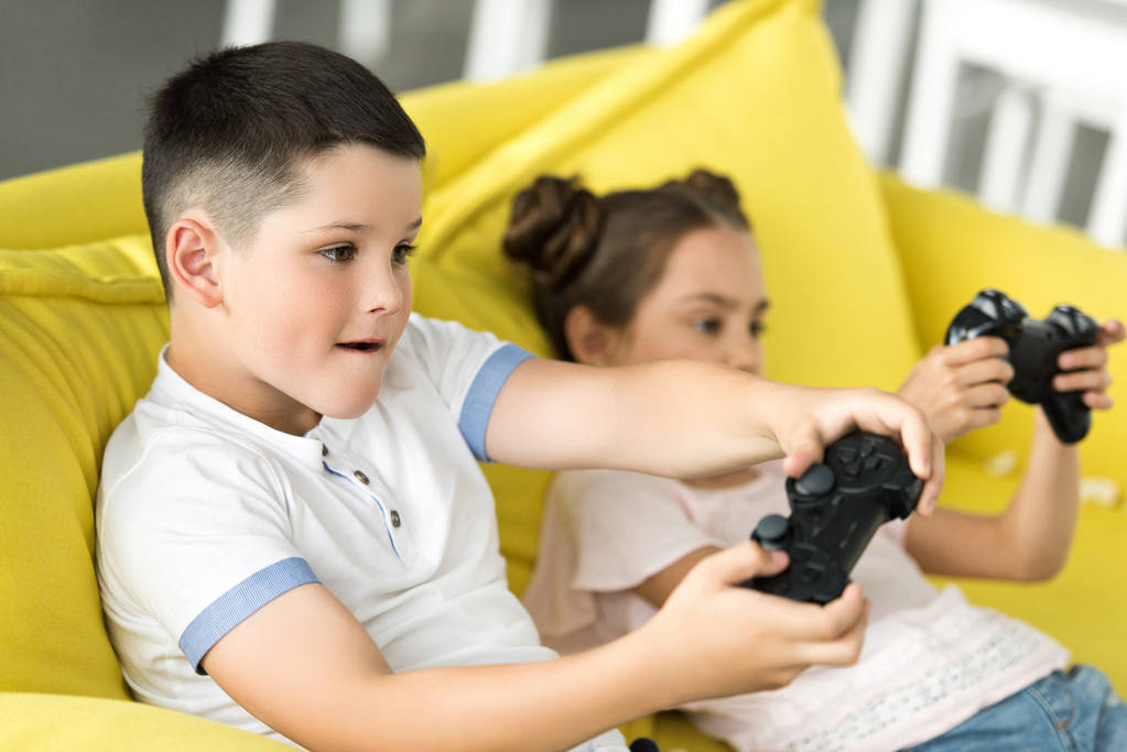 siblings playing video game on sofa at home - Photo, Image