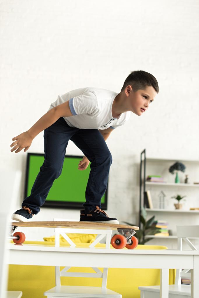 pre-adolescente jongen staande op skateboard op tafel thuis - Foto, afbeelding