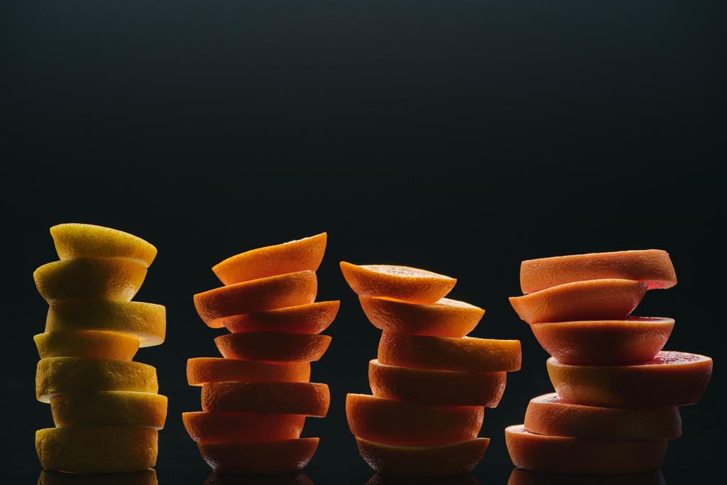 gestapelde segmenten van verschillende rijp citrus fruit plakjes geïsoleerd op zwart - Foto, afbeelding