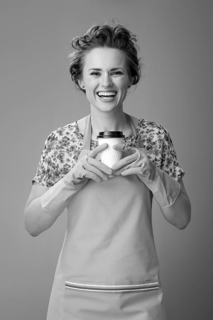 χαμογελώντας σύγχρονη νοικοκυρά σε μια ποδιά που κατέχει ένα φλυτζάνι καφέ - Φωτογραφία, εικόνα