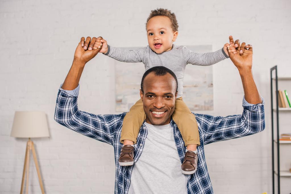 счастливый молодой отец носит очаровательного маленького сына на шее и улыбается в камеру
 - Фото, изображение