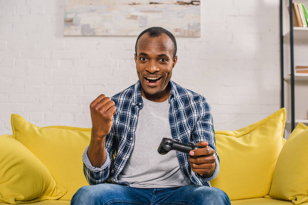 joystick ile evde oynarken kameraya gülümseyen neşeli Afrikalı-Amerikalı adam - Fotoğraf, Görsel