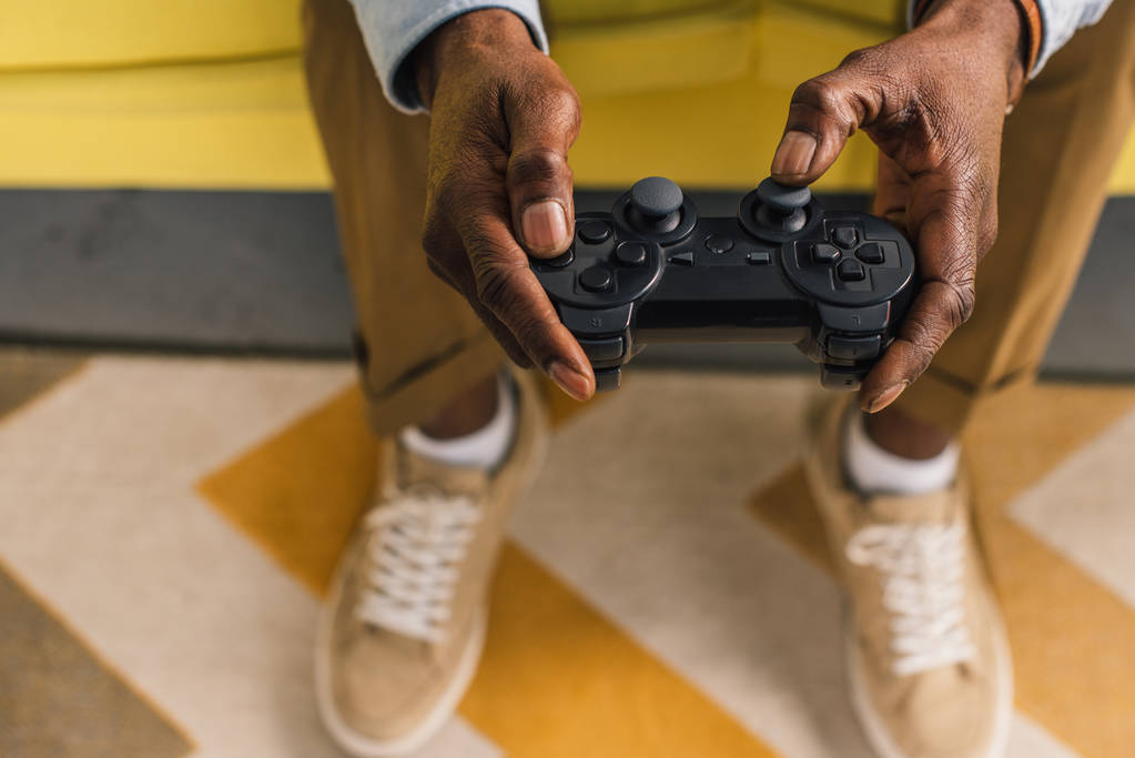 bijgesneden schot van Afro-Amerikaanse man zittend op de Bank en spelen met joystick - Foto, afbeelding