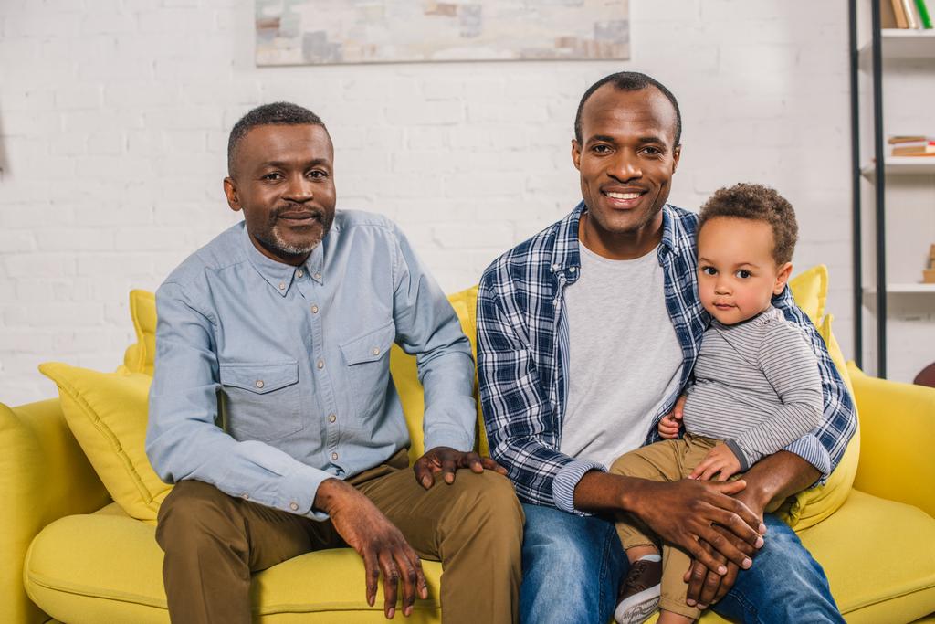 щасливий афроамериканський батько, дід і дитина сидять разом і дивляться на камеру
 - Фото, зображення