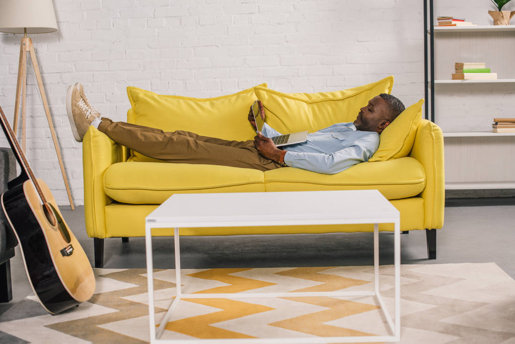 homem americano africano sênior deitado no sofá e usando laptop
 - Foto, Imagem