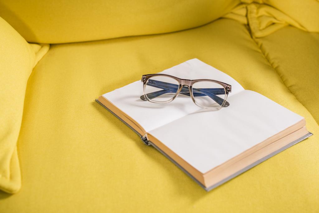 close-up view of eyeglasses and book with blank pages on yellow couch - Photo, Image