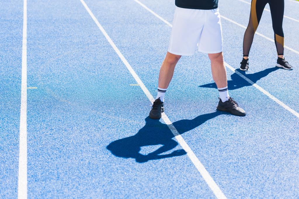 recortado disparo de hombre y mujer en ropa deportiva moderna de pie en pista de atletismo
 - Foto, imagen