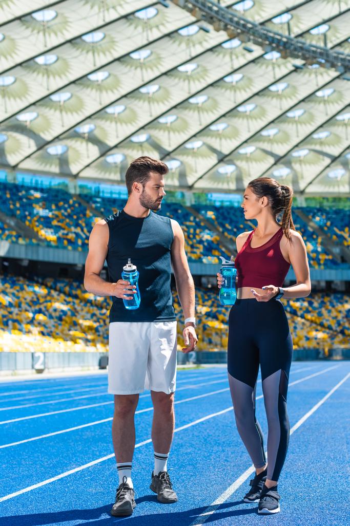 Młoda sportive para z butelki wody, stojąc na bieżnię o stadion sportowy i mówienie - Zdjęcie, obraz