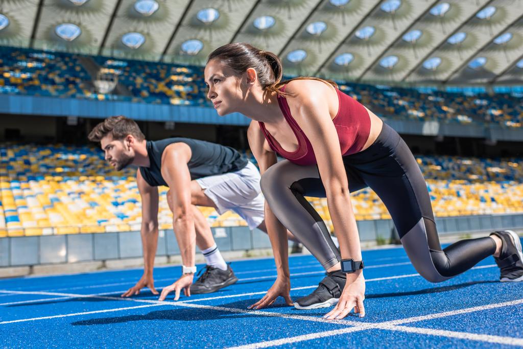 sportif genç erkek ve dişi sprinters içinde koşu parkuru, spor stadyum üzerinde başlangıç - Fotoğraf, Görsel