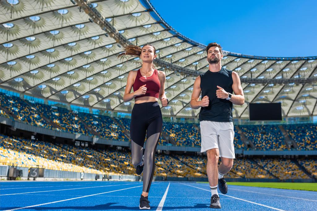 vista inferior de joggers jóvenes masculinos y femeninos corriendo en pista en el estadio deportivo
 - Foto, Imagen