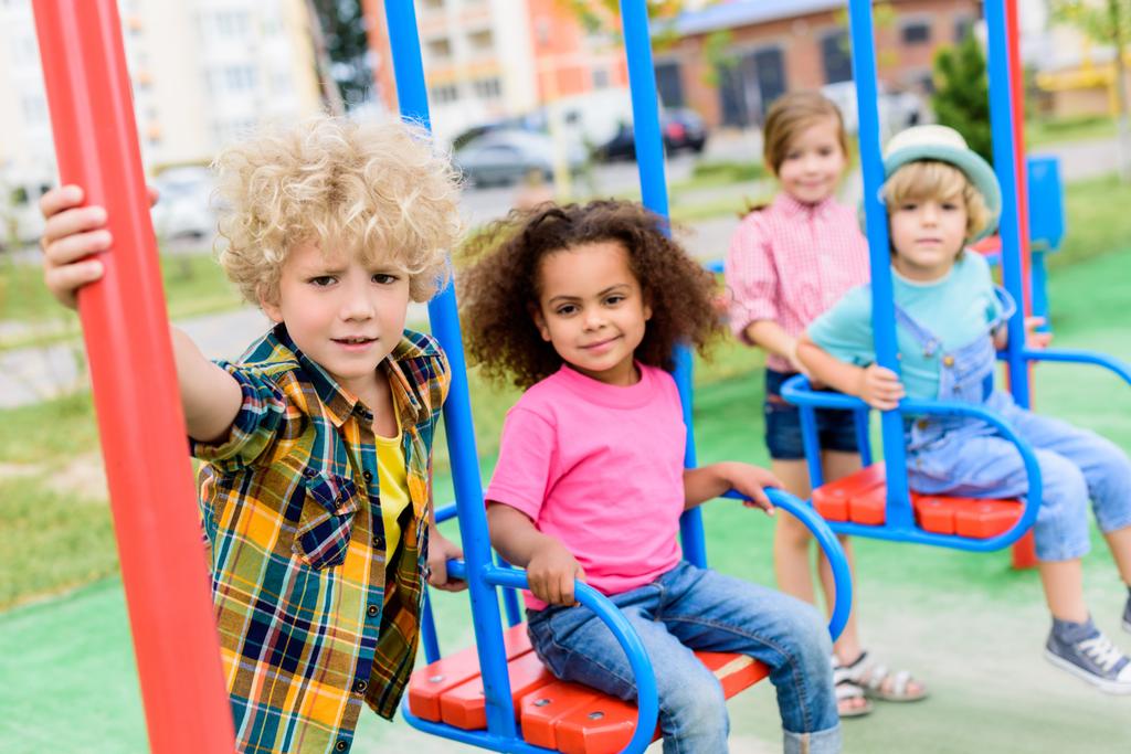 мультикультурна група маленьких дітей, які катаються на гойдалках на дитячому майданчику
  - Фото, зображення