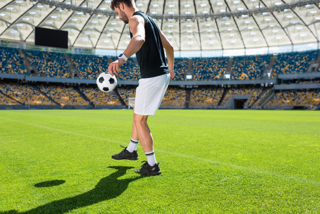 pohledný mladý fotbalista skákací míč na noze na sportovní stadion - Fotografie, Obrázek