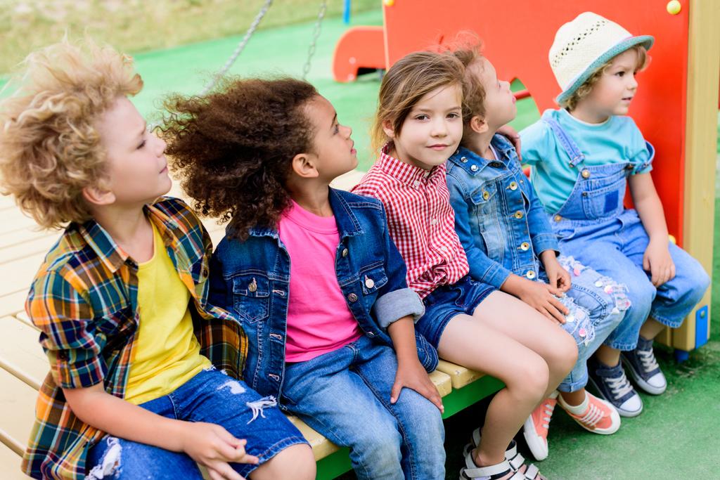 felici bambini multietnici seduti insieme al parco giochi
  - Foto, immagini