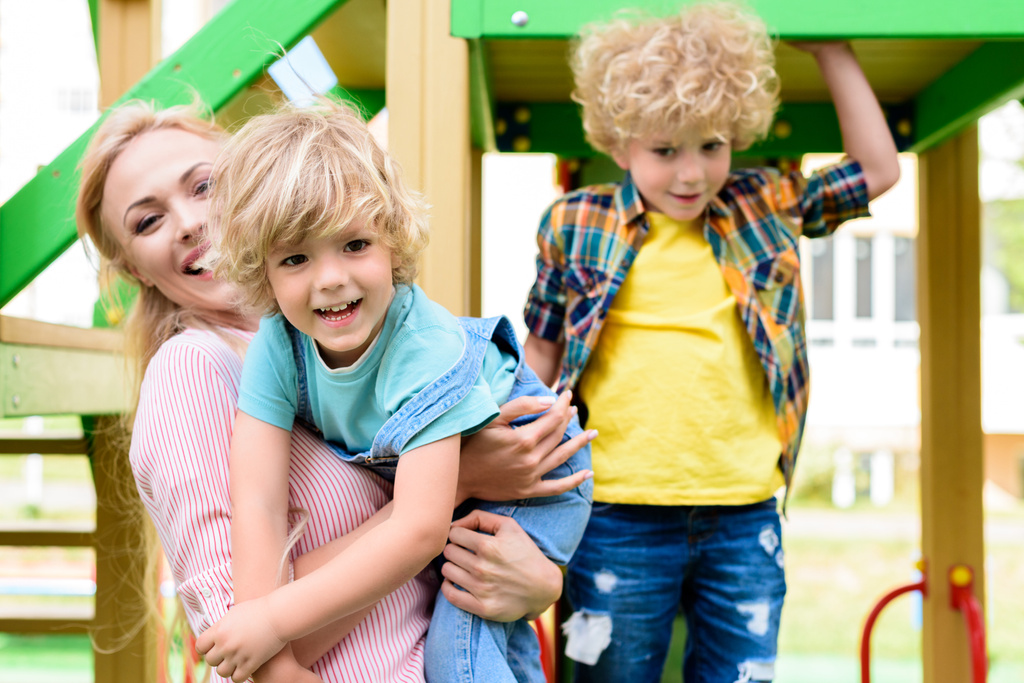 mãe feliz com dois adoráveis meninos brincalhões no parque infantil
  - Foto, Imagem