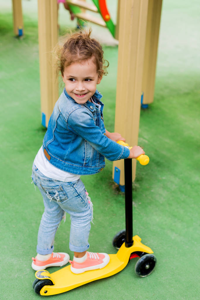 hoge hoekmening van klein kind rijden op kick scooter op speelplaats  - Foto, afbeelding