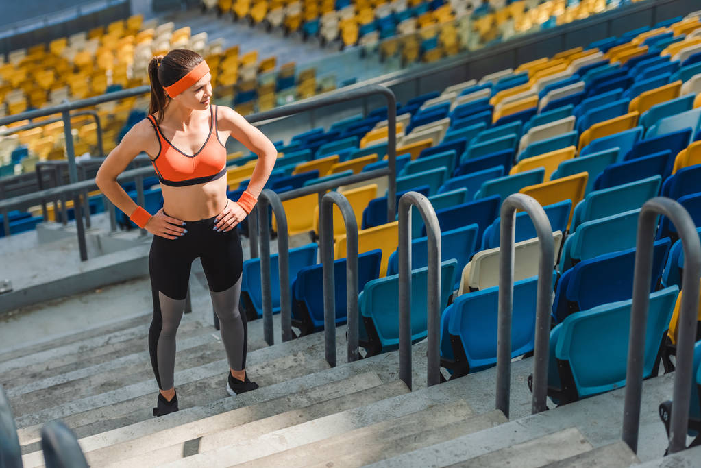 высокий угол обзора спортивной молодой женщины, стоящей на лестнице на спортивном стадионе с оружием акимбо
 - Фото, изображение