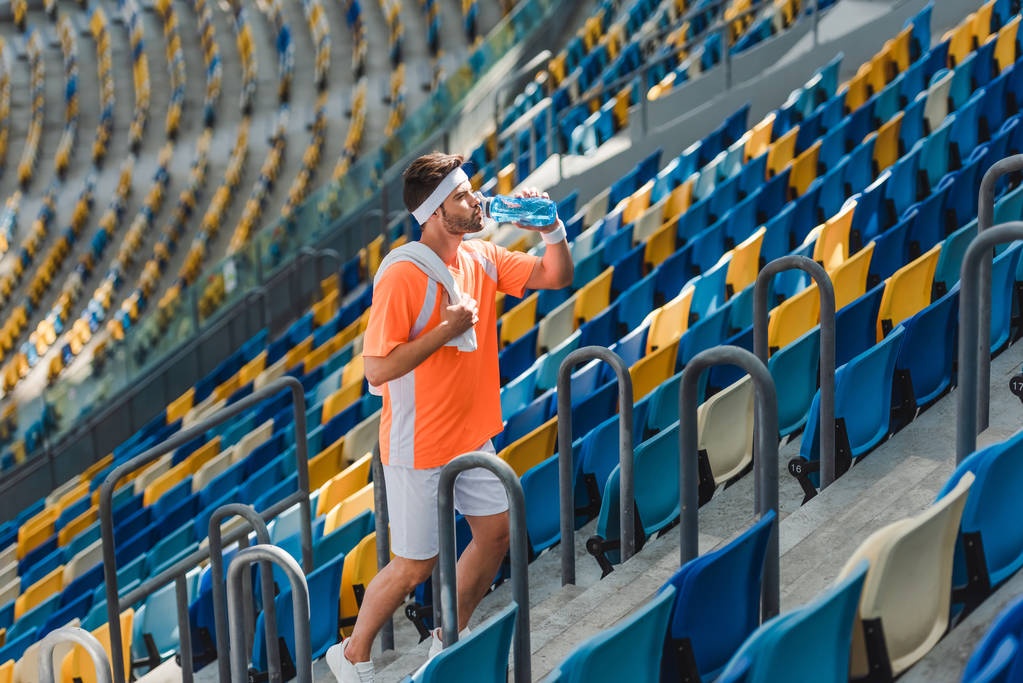 unavený mladého sportovce pitné vody na schodech na sportovní stadion - Fotografie, Obrázek