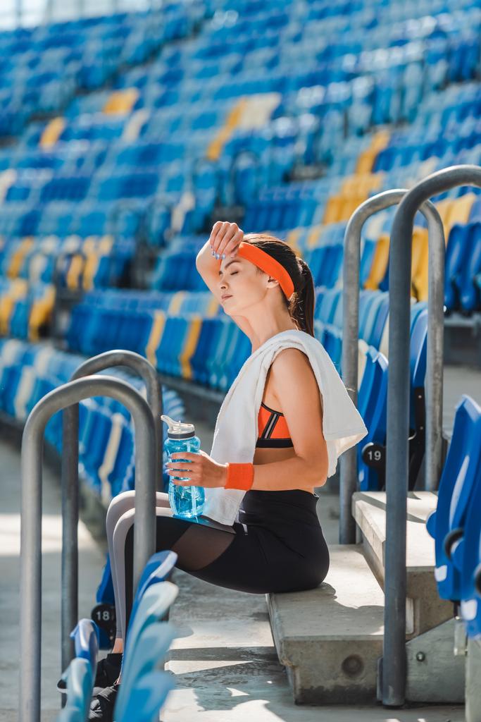 sivunäkymä väsynyt nuori nainen rentouttava portailla ja pyyhkimällä hiki urheilustadionilla
 - Valokuva, kuva