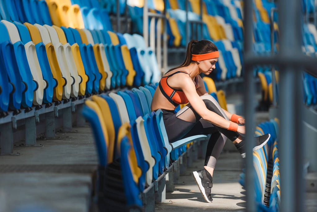 вид сбоку спортивной молодой женщины, сидящей на трибунах на спортивном стадионе
 - Фото, изображение