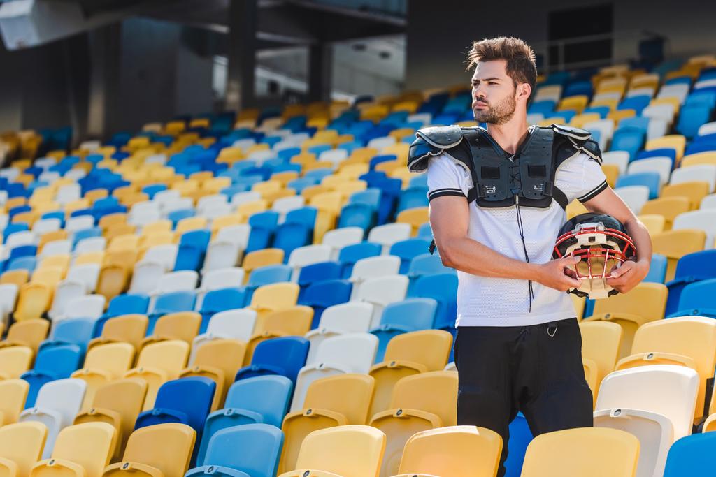 bello giovane giocatore di football americano in attrezzature in piedi su tribune allo stadio sportivo
 - Foto, immagini