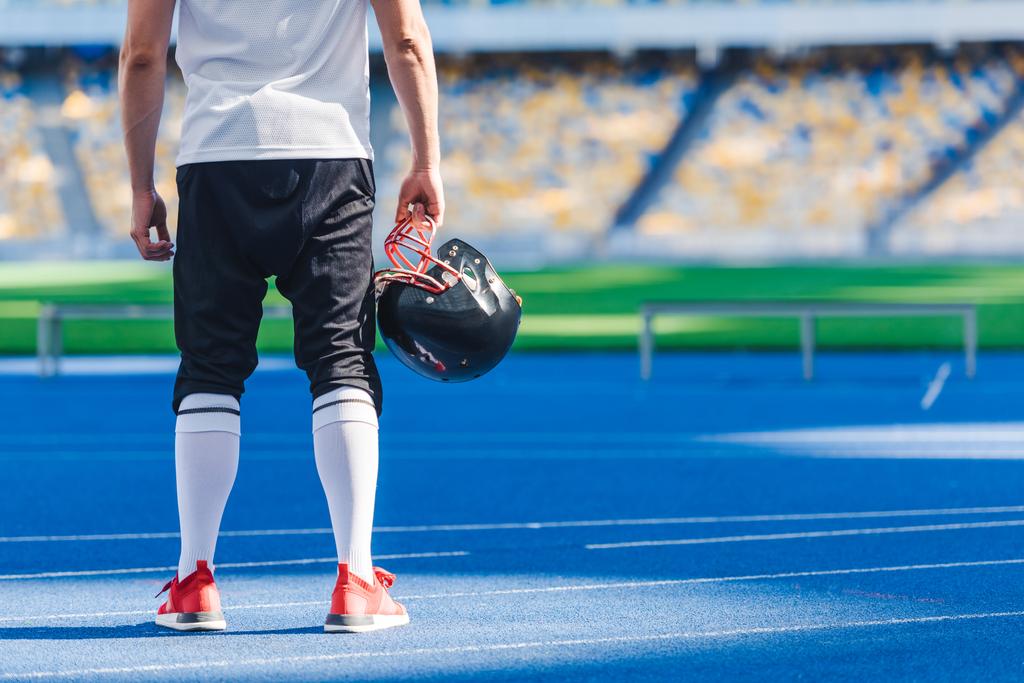 tiro recortado de jogador de futebol americano com capacete em pé sozinho no estádio de esportes
 - Foto, Imagem