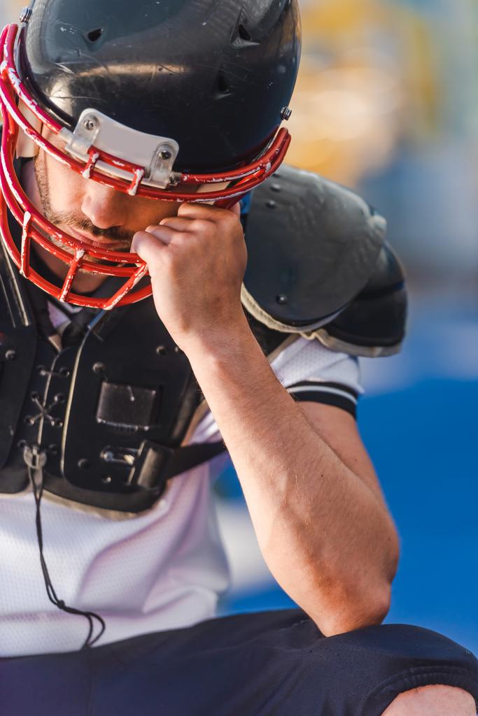 молодой американский футболист, держащий в руках клетку шлема, сидя на спортивном стадионе
 - Фото, изображение