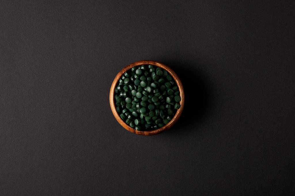 pohled shora dřevěná miska s hromadou spirulina tablety na šedý stůl  - Fotografie, Obrázek