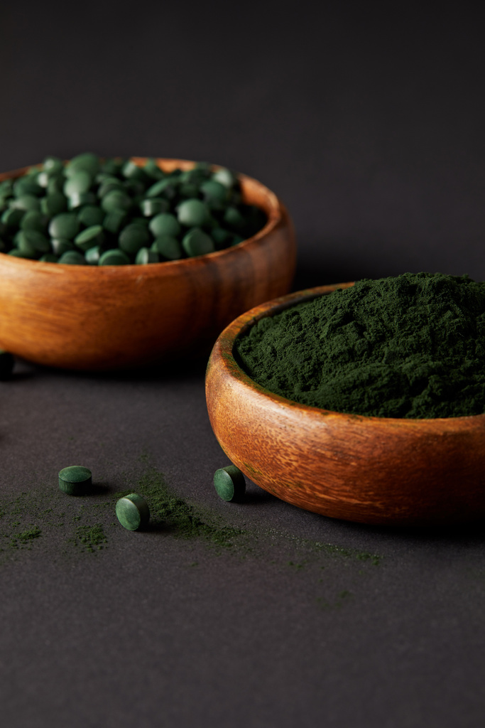 close up view of wooden bowls with ground spirulina and spirulina in pills on grey table  - Photo, Image